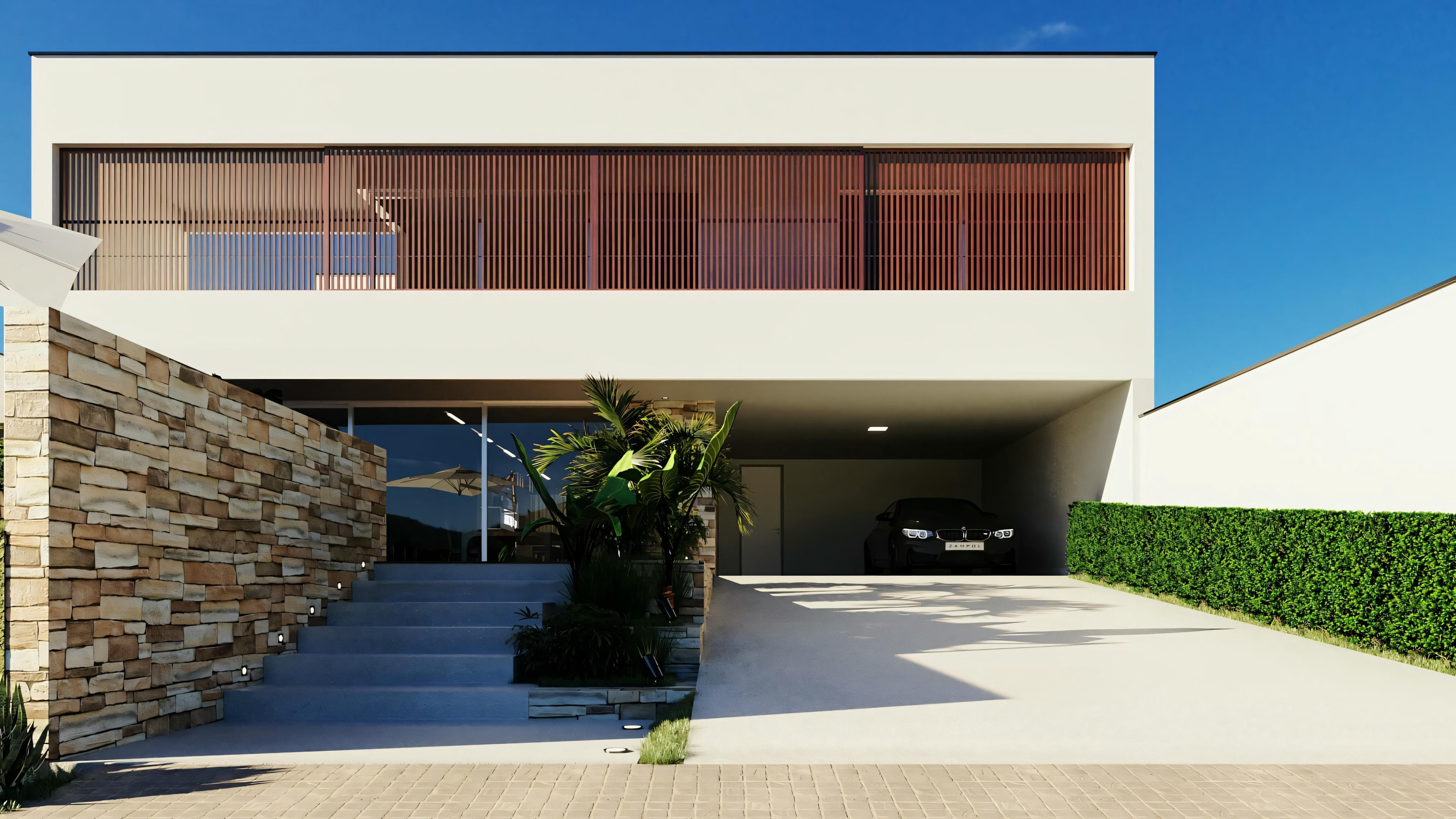 A modern two-story house with a flat roof, large windows, and a balcony with a glass railing. The facade combines white walls and wood panels, with visible landscaping in the form of well-kept lawns and a stone wall leading to the entrance.