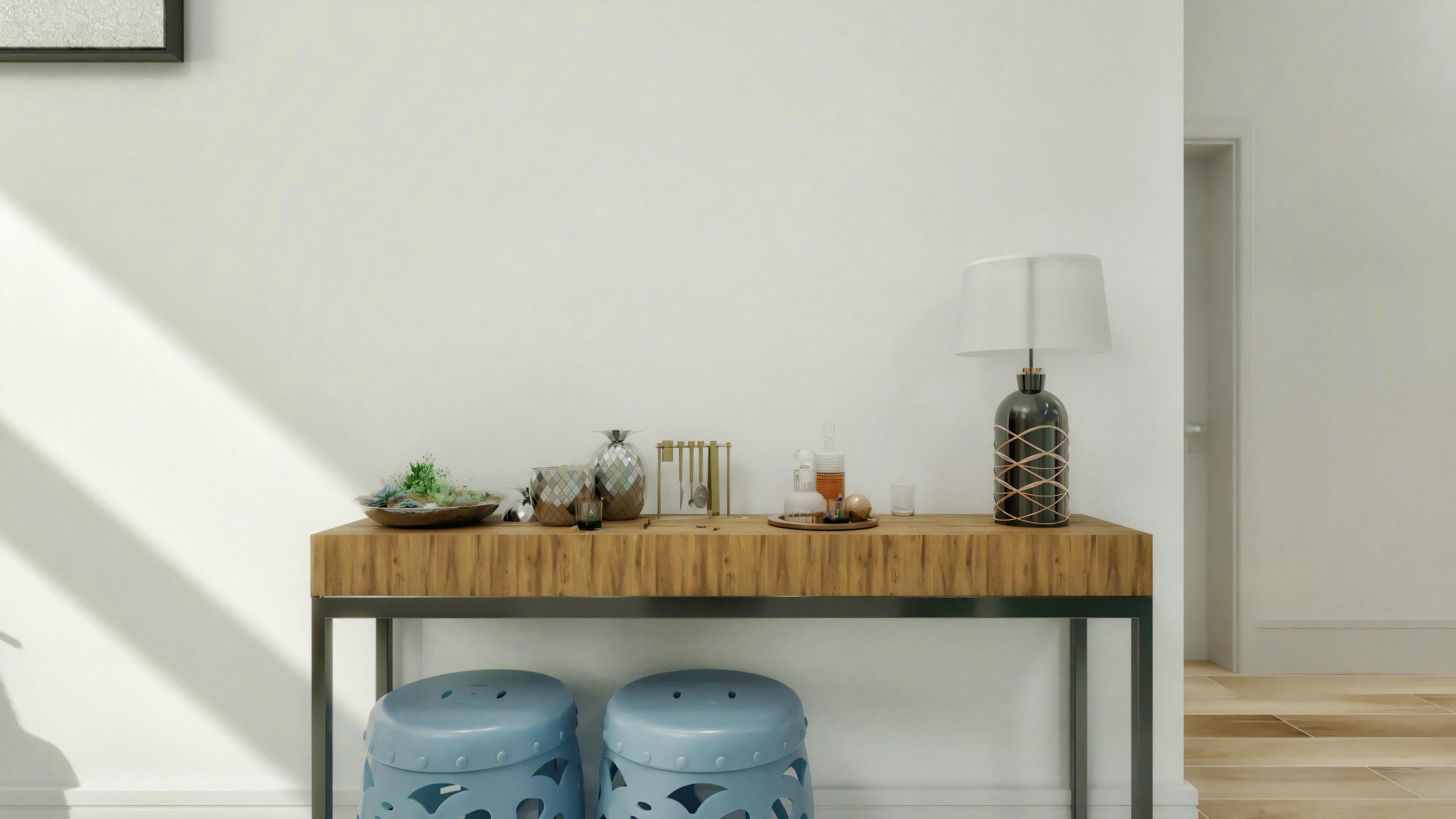 Una sala con pared clara y borde superior con patrón oscuro, mesa de consola de madera con objetos decorativos y taburetes azules.