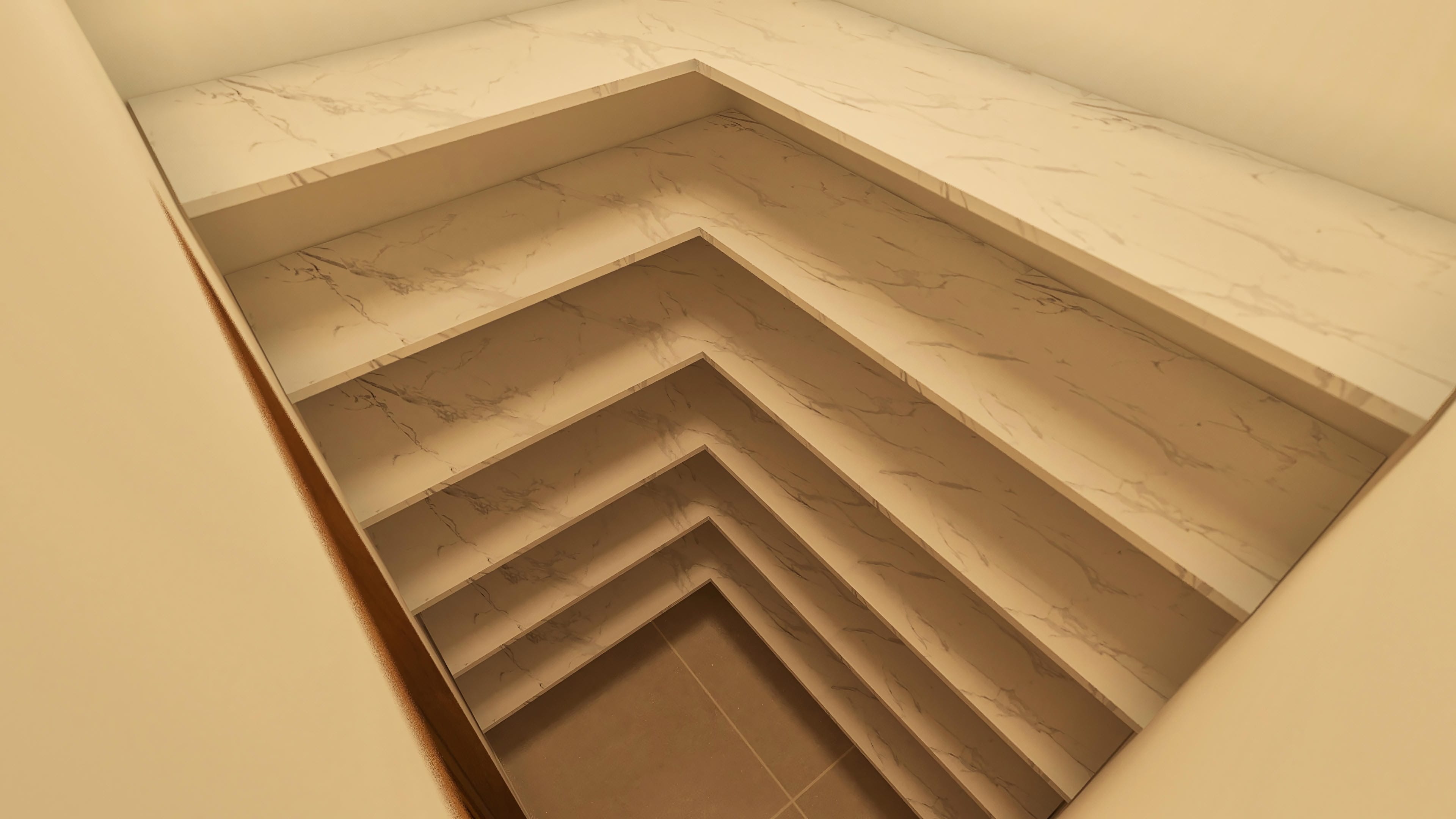 Detalle de estanterías modernas con revestimiento en mármol, organizadas en niveles escalonados, en tonos neutros y elegantes.