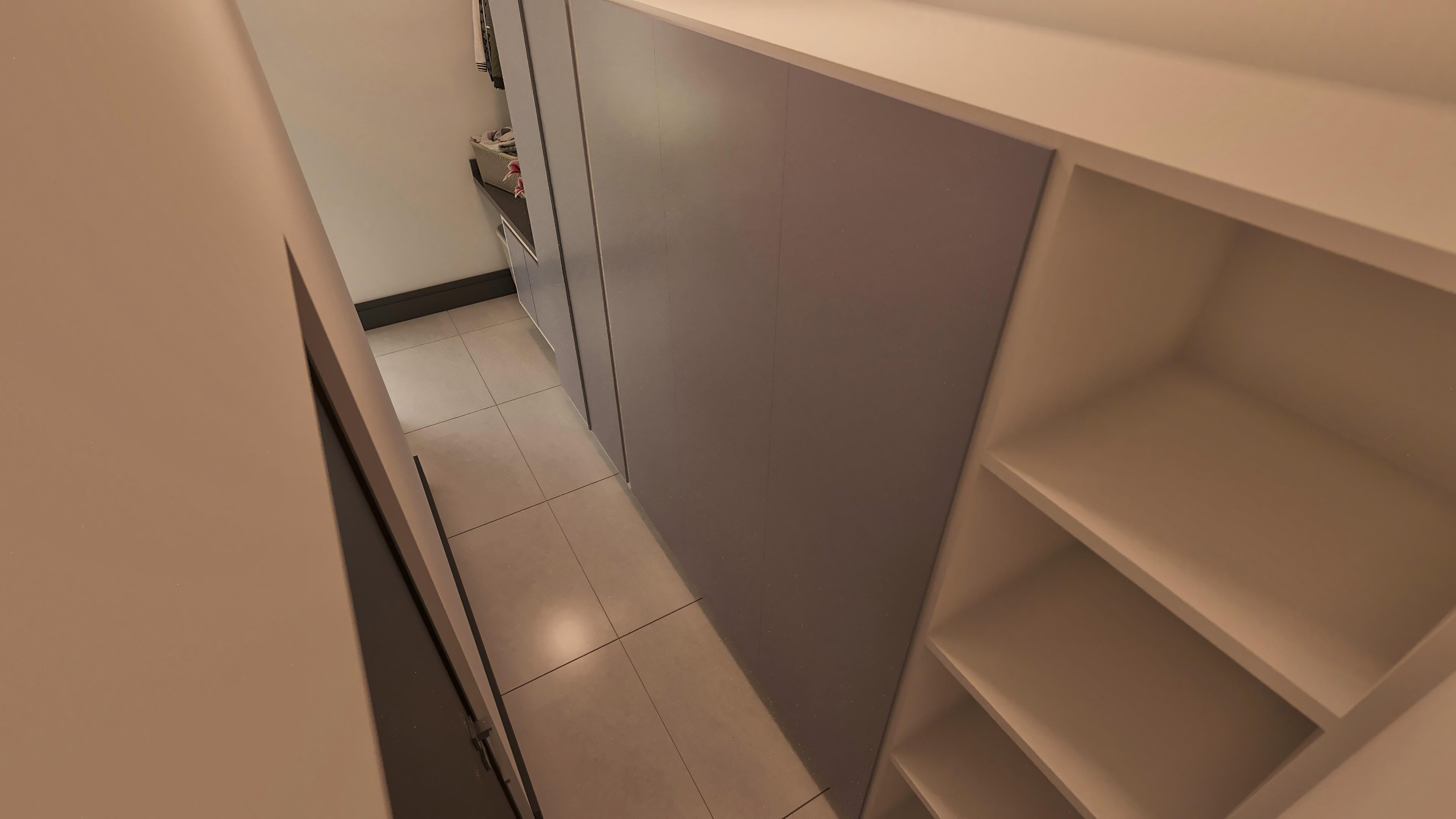 Interior moderno com piso em porcelanato de grandes formatos, armários planejados em tons neutros e prateleiras embutidas, evidenciando organização e sofisticação.