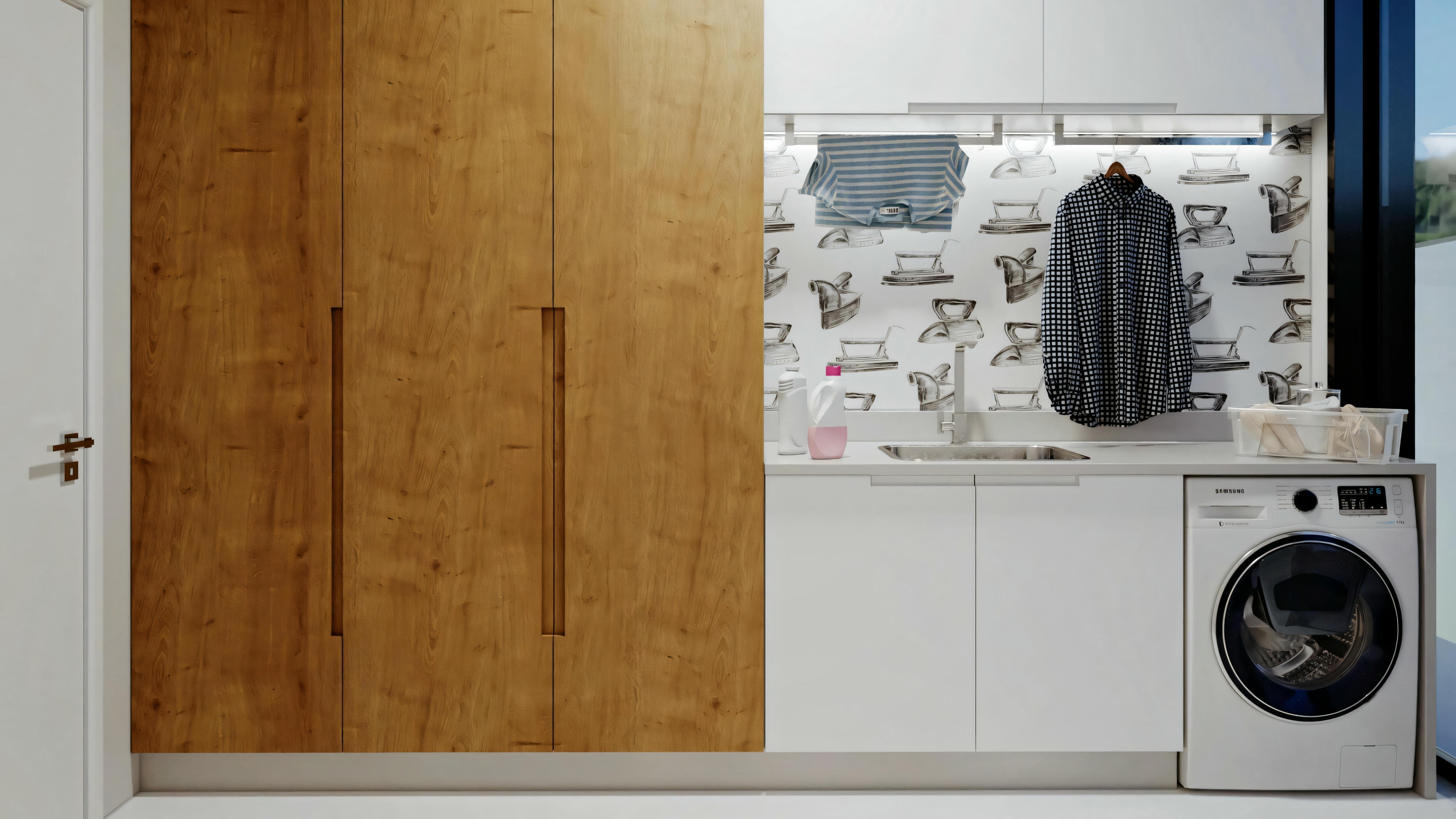 A laundry room with a washing machine, wooden door, and tiled walls. A black and white cat is sitting on the washing machine.