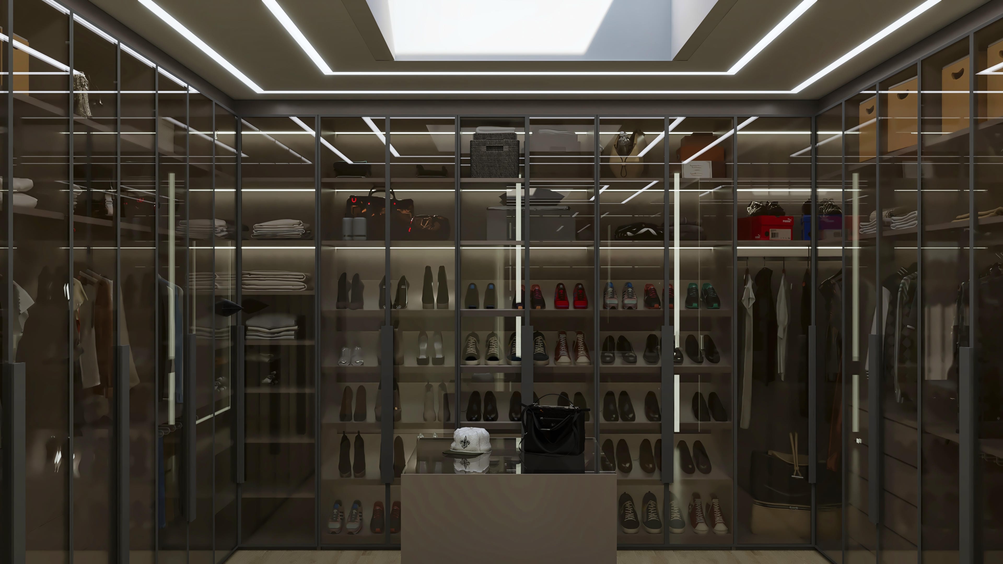 Interior de um closet de alto padrão com armários de vidro fumê, iluminação embutida e organização de roupas e sapatos.