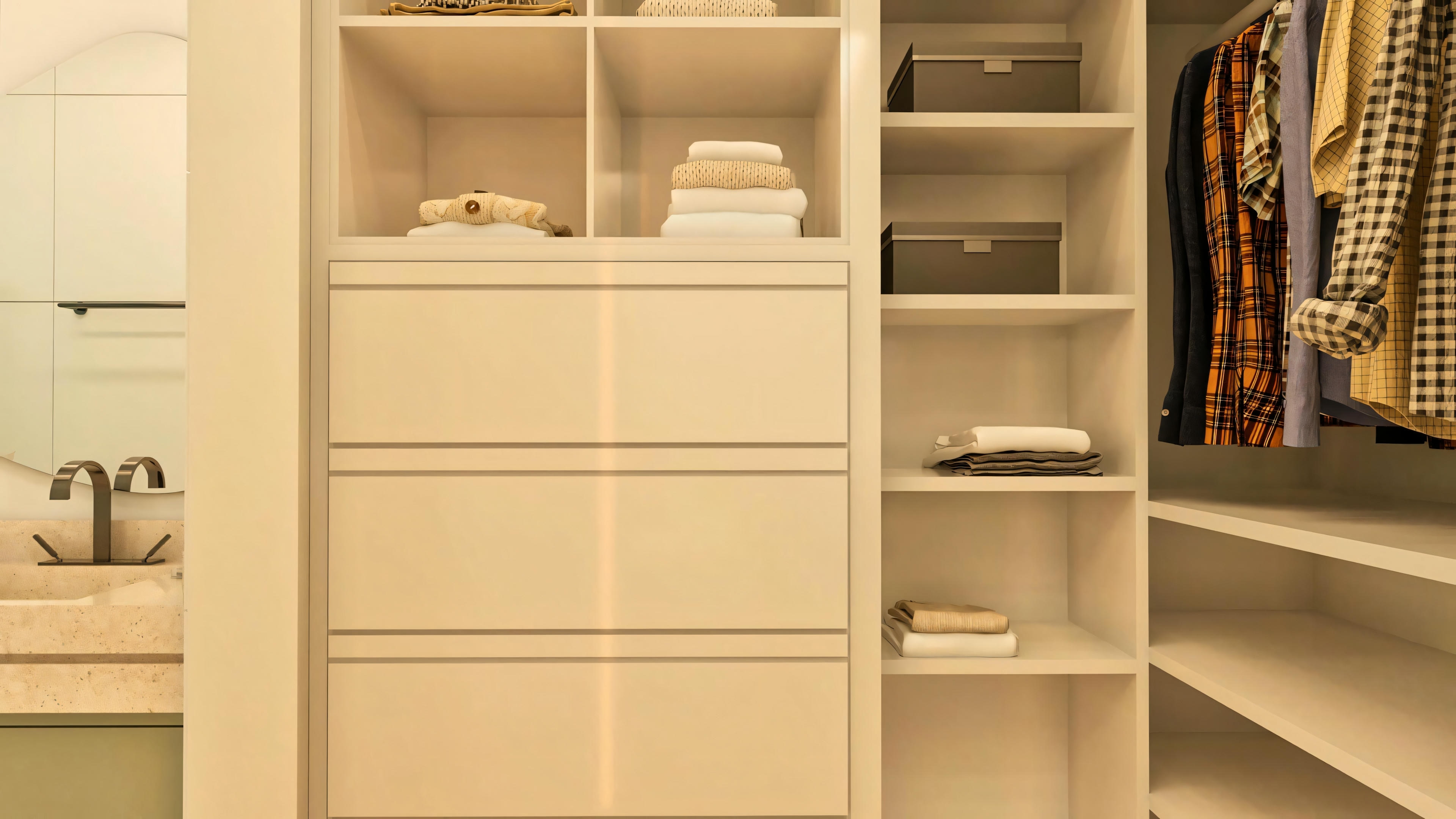 Detalhe do closet em suíte de casa de luxo, com armários planejados brancos, gavetas, prateleiras e parte de banheiro adjacente.