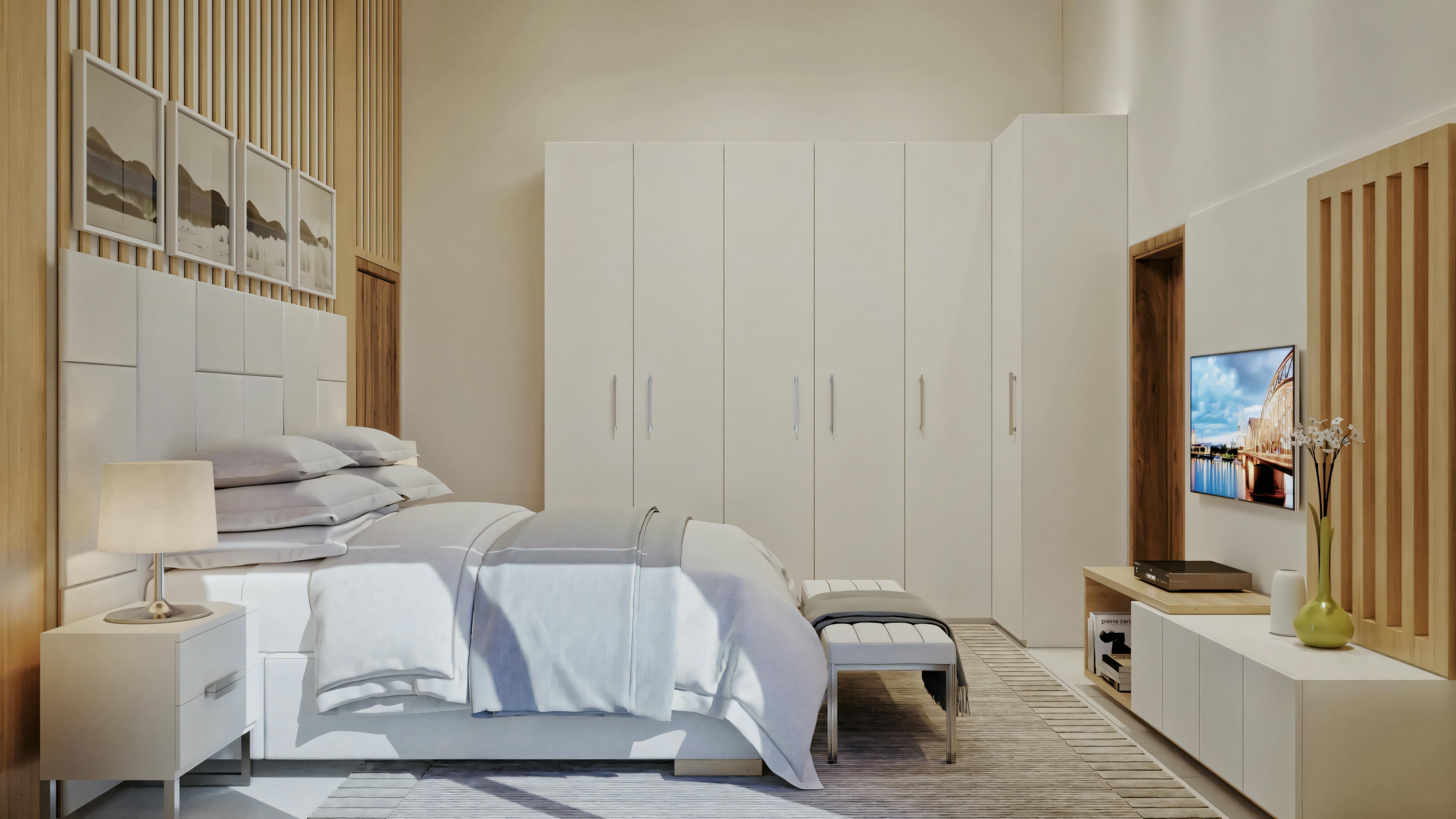 Um quarto com uma cama grande, roupa de cama branca, vários travesseiros, mesa de cabeceira com livros, quadros na parede e uma poltrona no canto.