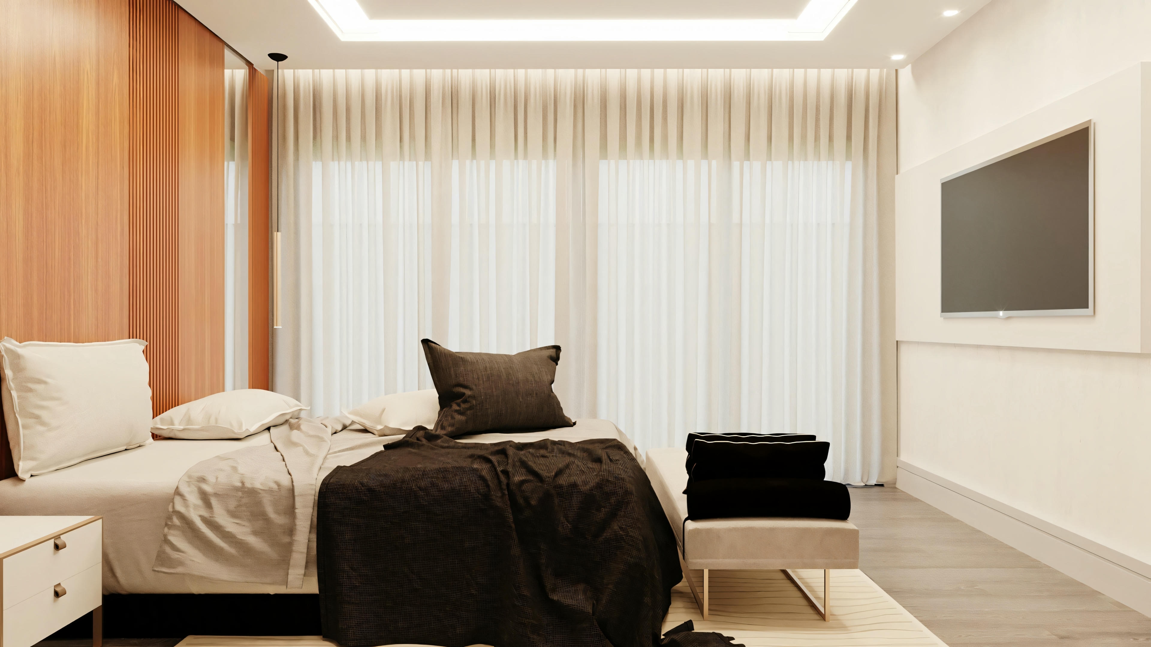 A modern bedroom with a large bed in the center, two pillows, and a black blanket at the foot. There is a flat-screen TV mounted on the wall opposite the bed, and white curtains behind it.