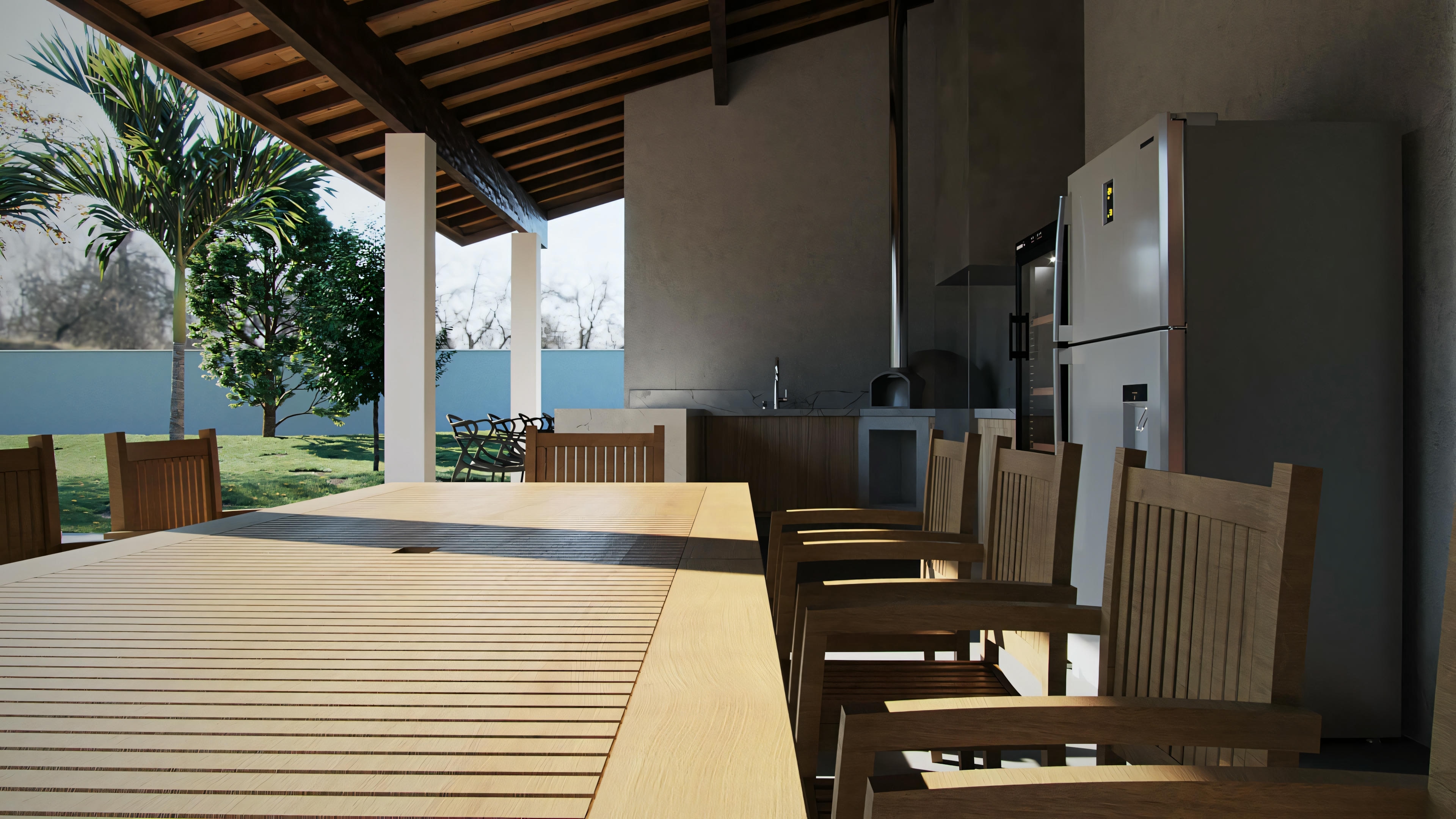 Un área de patio al aire libre con piso de madera, mesa de comedor larga con varias sillas y un área de cocina abierta al fondo.