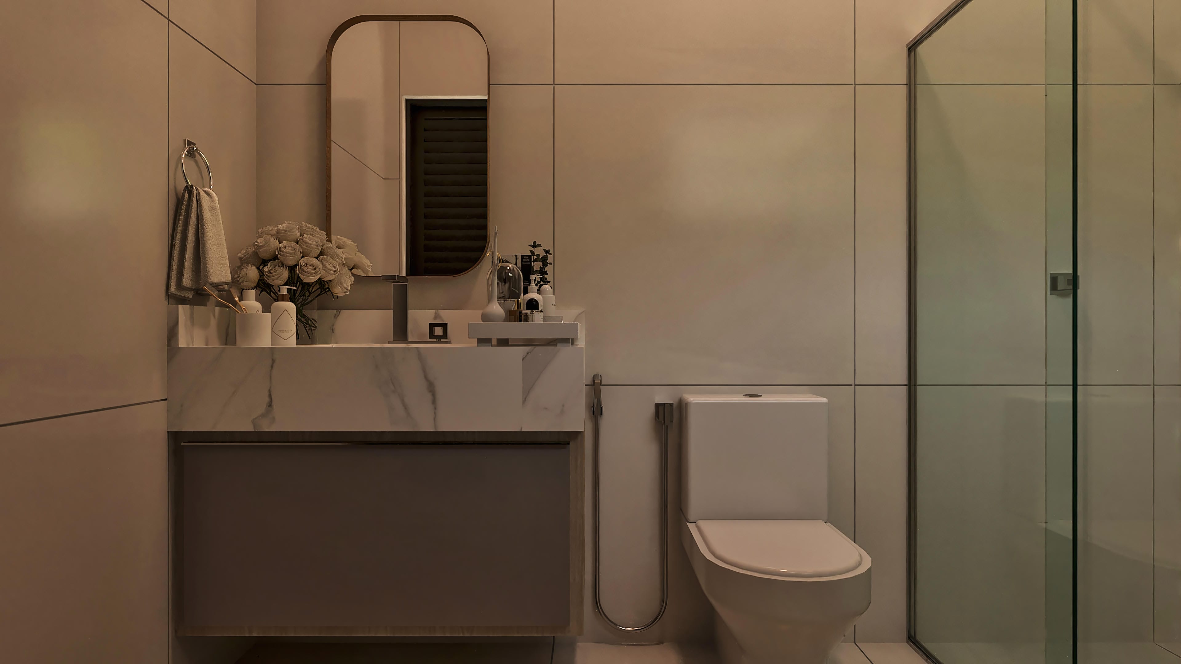 Detalle de baño moderno con revestimiento en grandes placas de porcelanato gris, encimera de mármol con lavabo esculpido y espejo con marco redondeado.