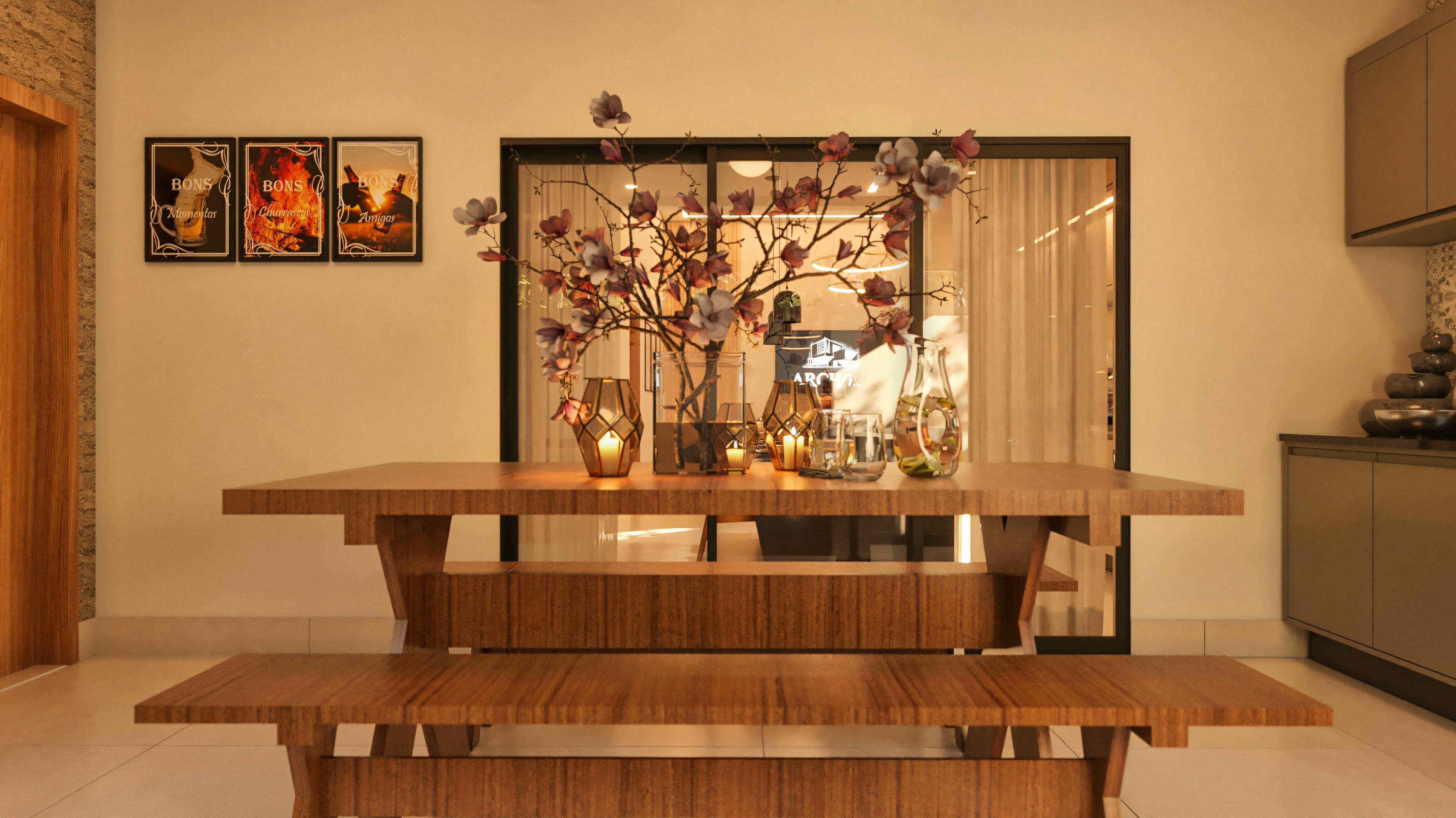 Mesa de jantar em madeira na área gourmet de uma casa moderna com 3 quartos, decorada com arranjos florais e velas. Ao fundo, porta de vidro de acesso à cozinha e quadros decorativos na parede.