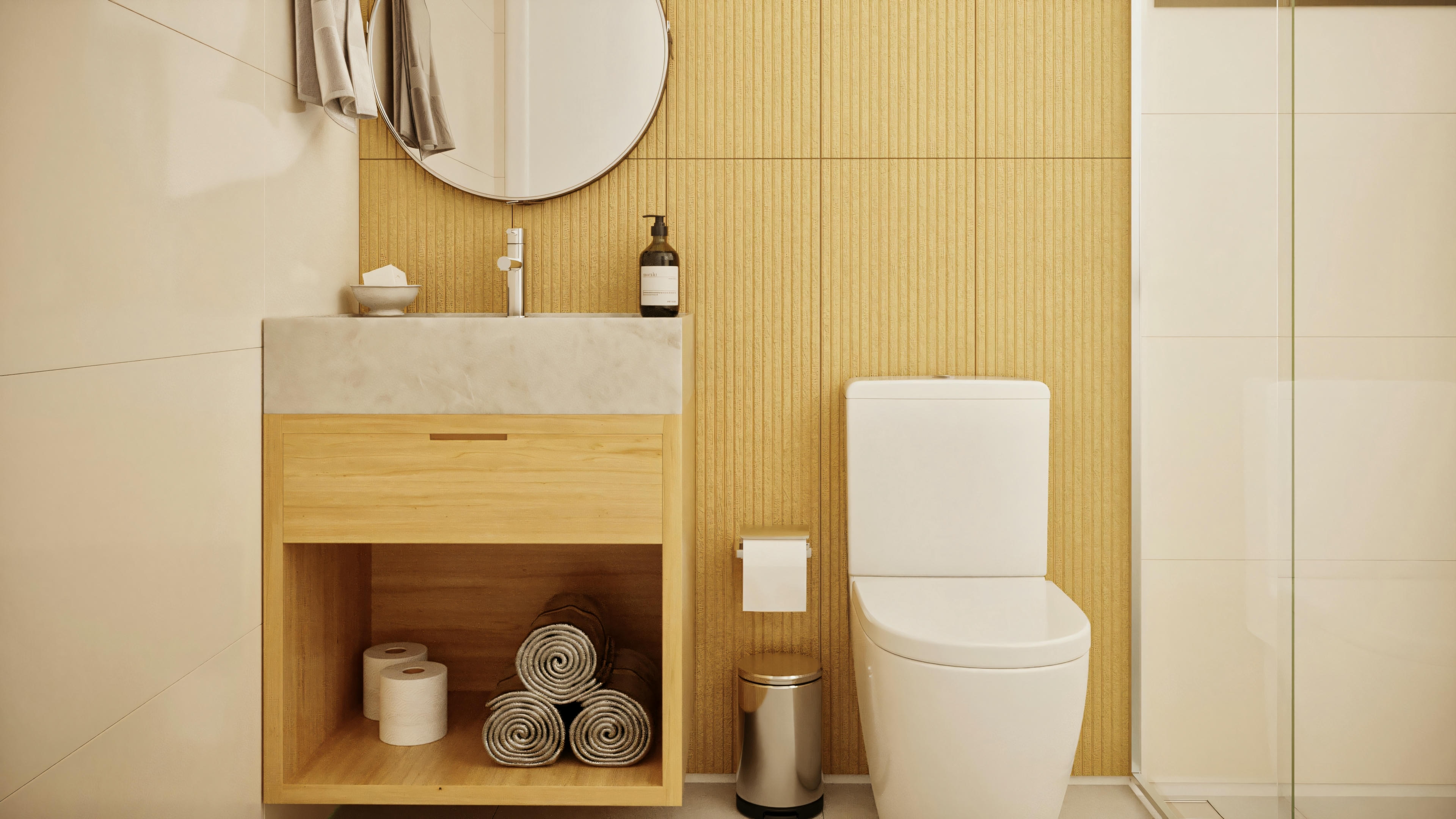 Baño con mueble de madera clara, lavabo de piedra, espejo redondo, inodoro y pared destacada con revestimiento amarillo texturizado.