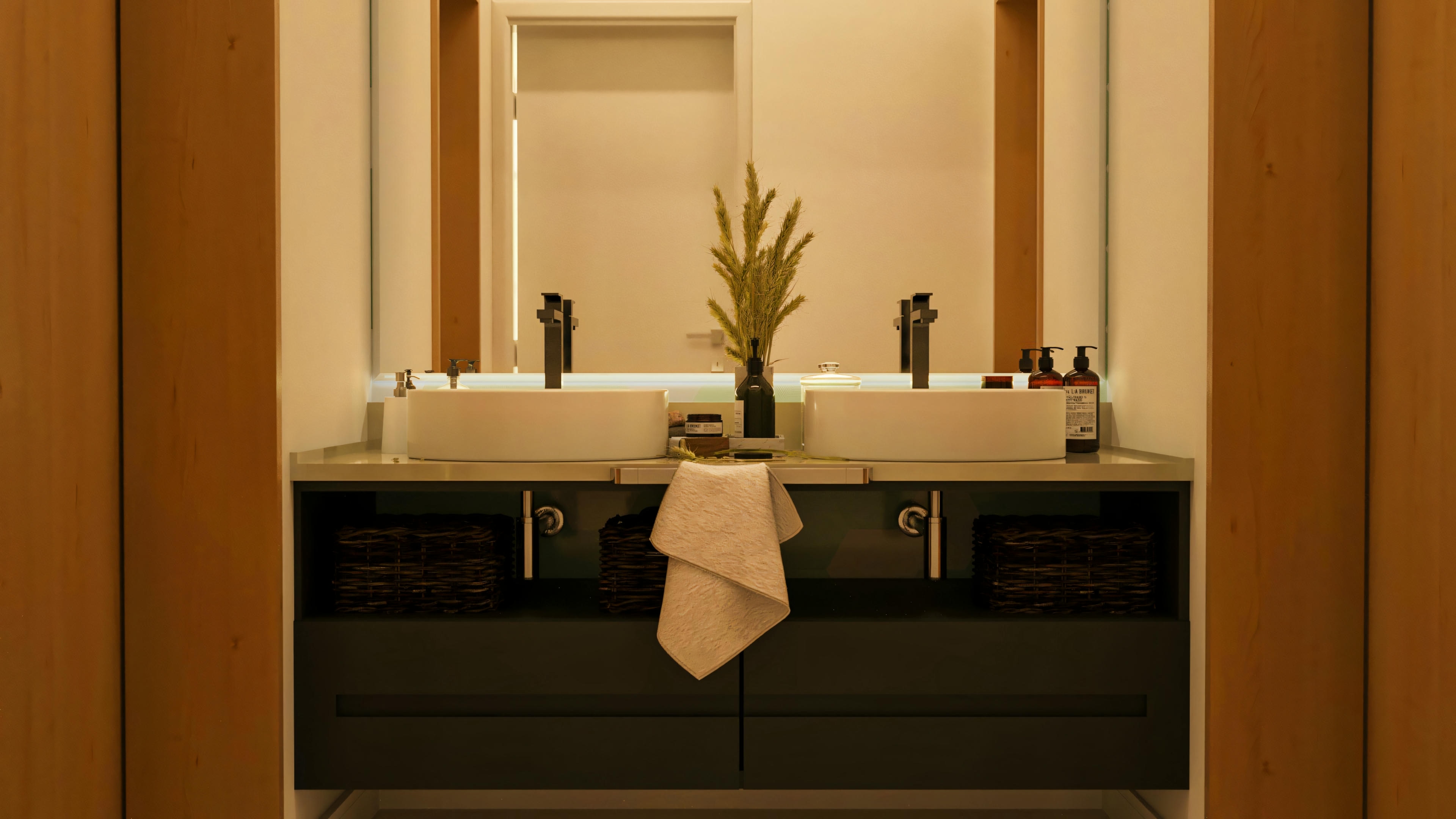 Baño de suite con mesada oscura, dos lavamanos de apoyo redondos blancos, grifería negra, mueble inferior con cajones y nichos con cestos, y amplio espejo con iluminación empotrada, en proyecto de casa con 5 baños.