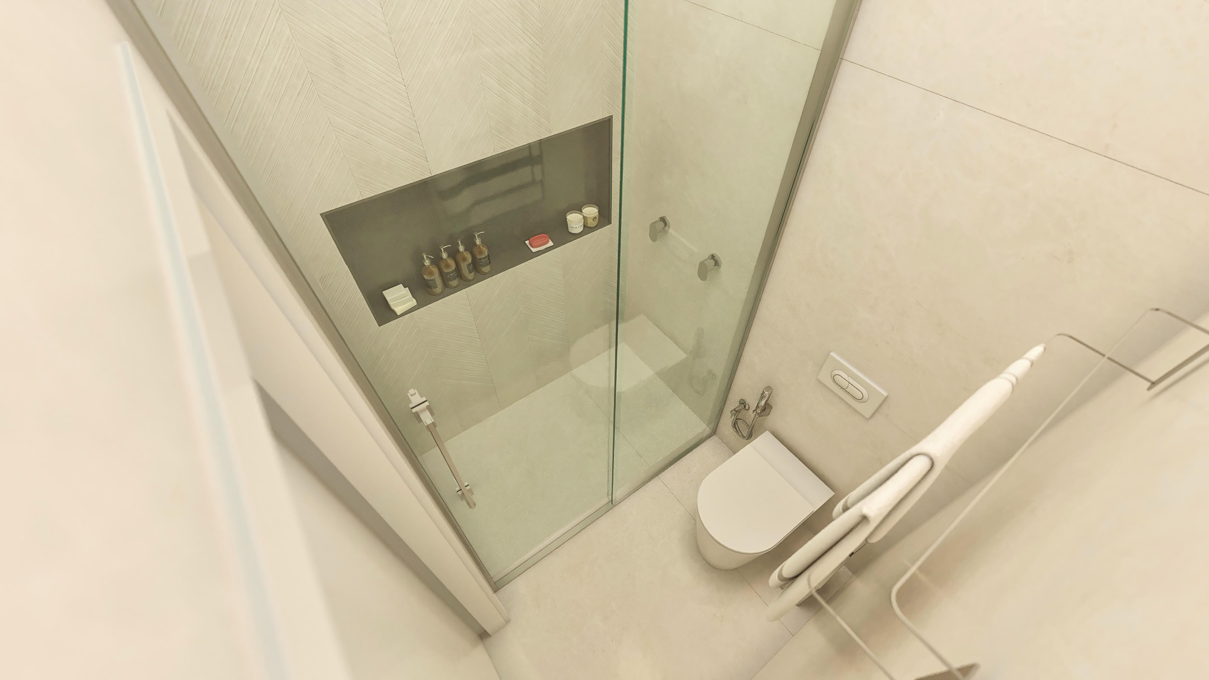 Interior of a high-end bathroom with textured herringbone cladding and neutral-toned countertop, with a glass shower enclosure and modern sanitary ware.