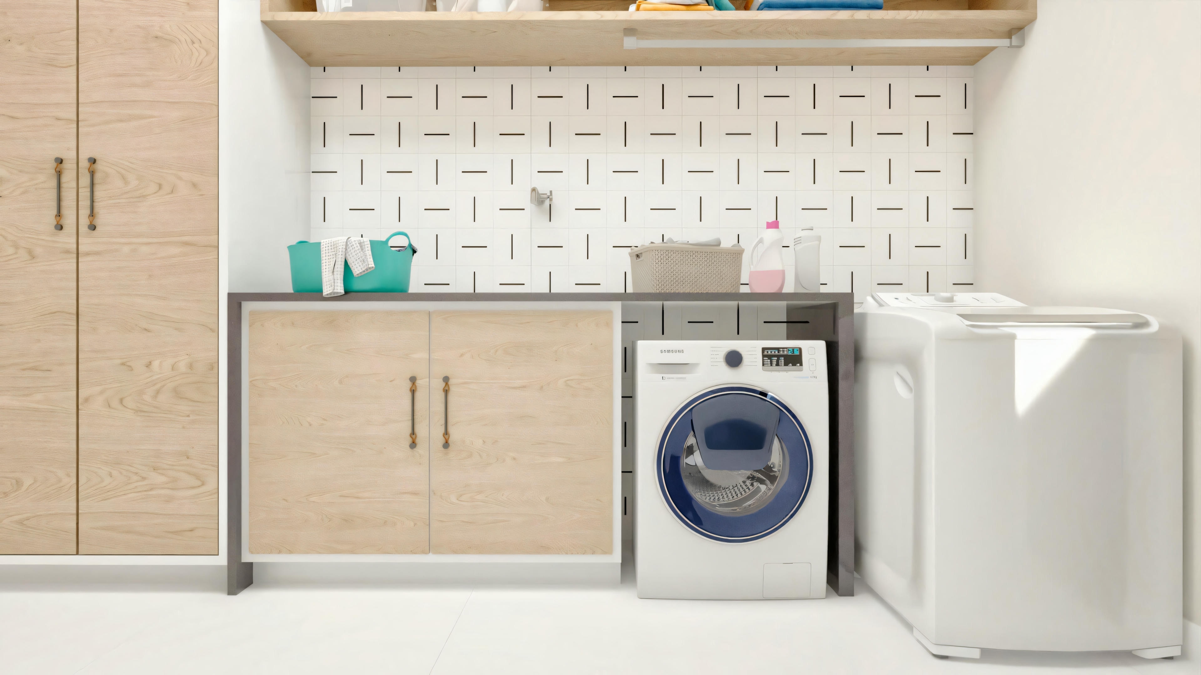 Laundry room of a ready-made project with 5 suites, with light wood planned cabinets, countertop, front-loading washing machine, space for a dryer, and wall covering with decorated white tiles.
