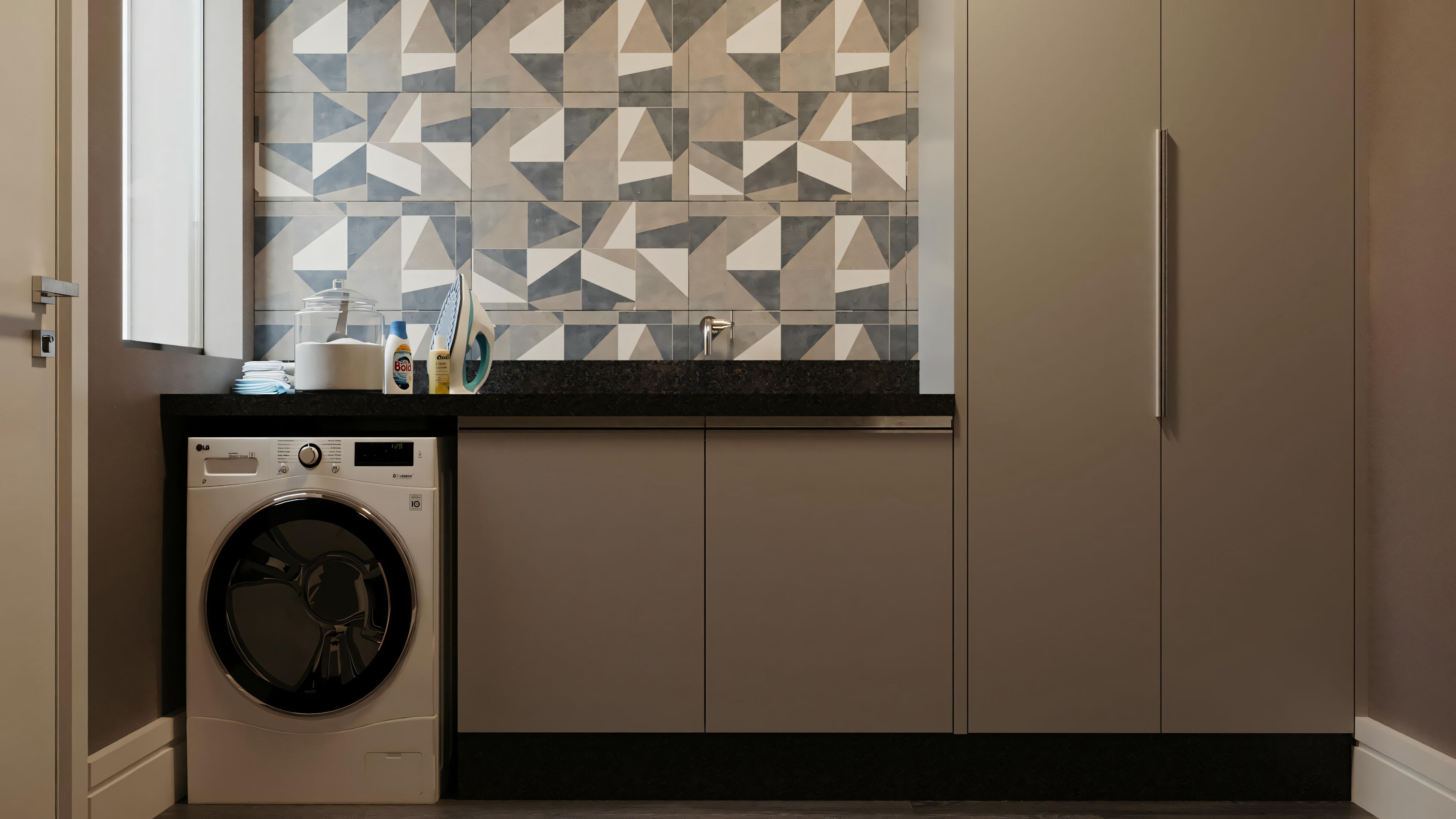 Lavandería con una lavadora bajo una encimera. La pared está adornada con azulejos geométricos y hay una puerta cerrada a la derecha.