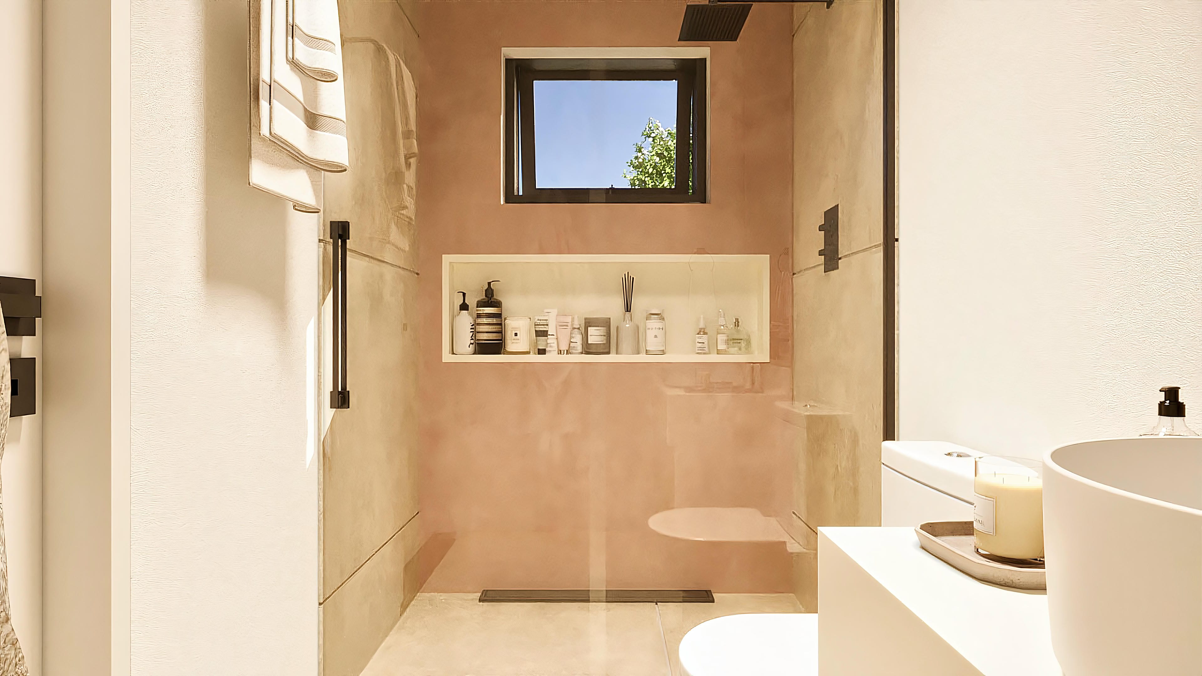 Encimera de baño con acabado en microcemento y nicho iluminado con productos de higiene y una pequeña ventana con vista al cielo y árboles.