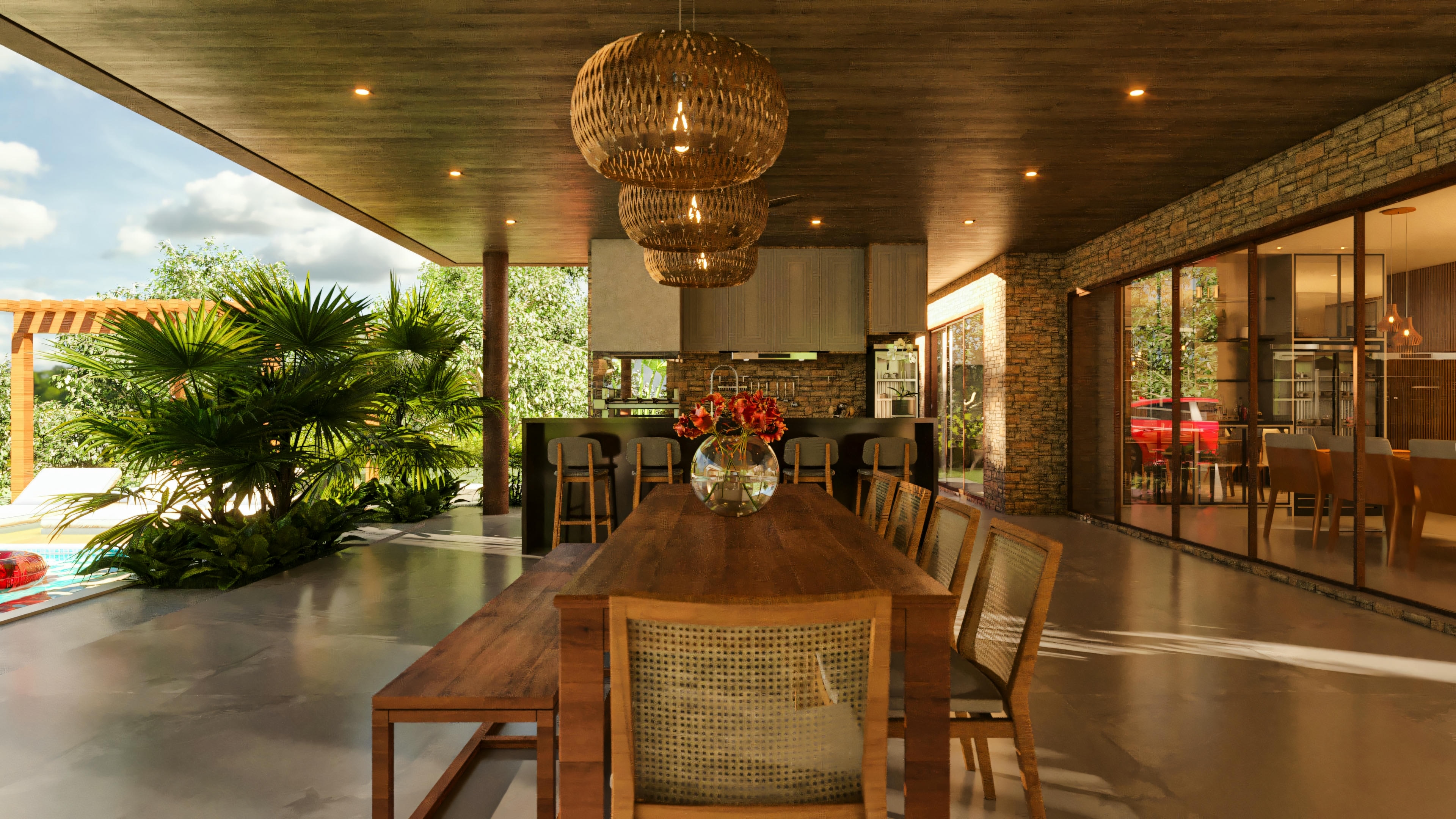 Amplia área gourmet y de comidas en casa de lujo, con mesa de comedor de madera, sillas con respaldo de mimbre, lámparas colgantes de fibra natural, encimera de bar al fondo y vista a la piscina y jardín.