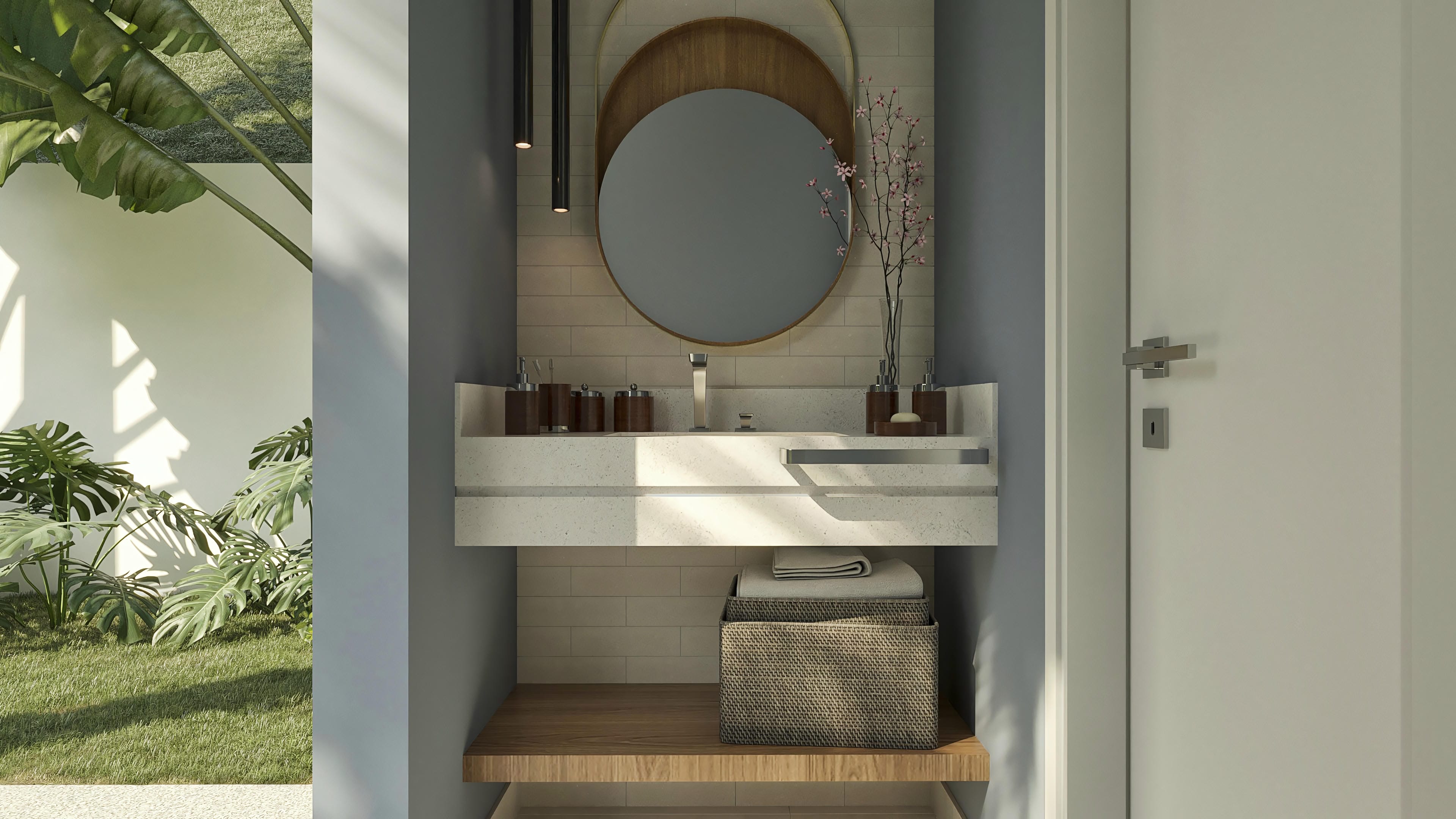 Bathroom interior with a modern countertop in light stone, a round mirror with a wooden frame, and pendant lighting. Accessories and vegetation complement the room.
