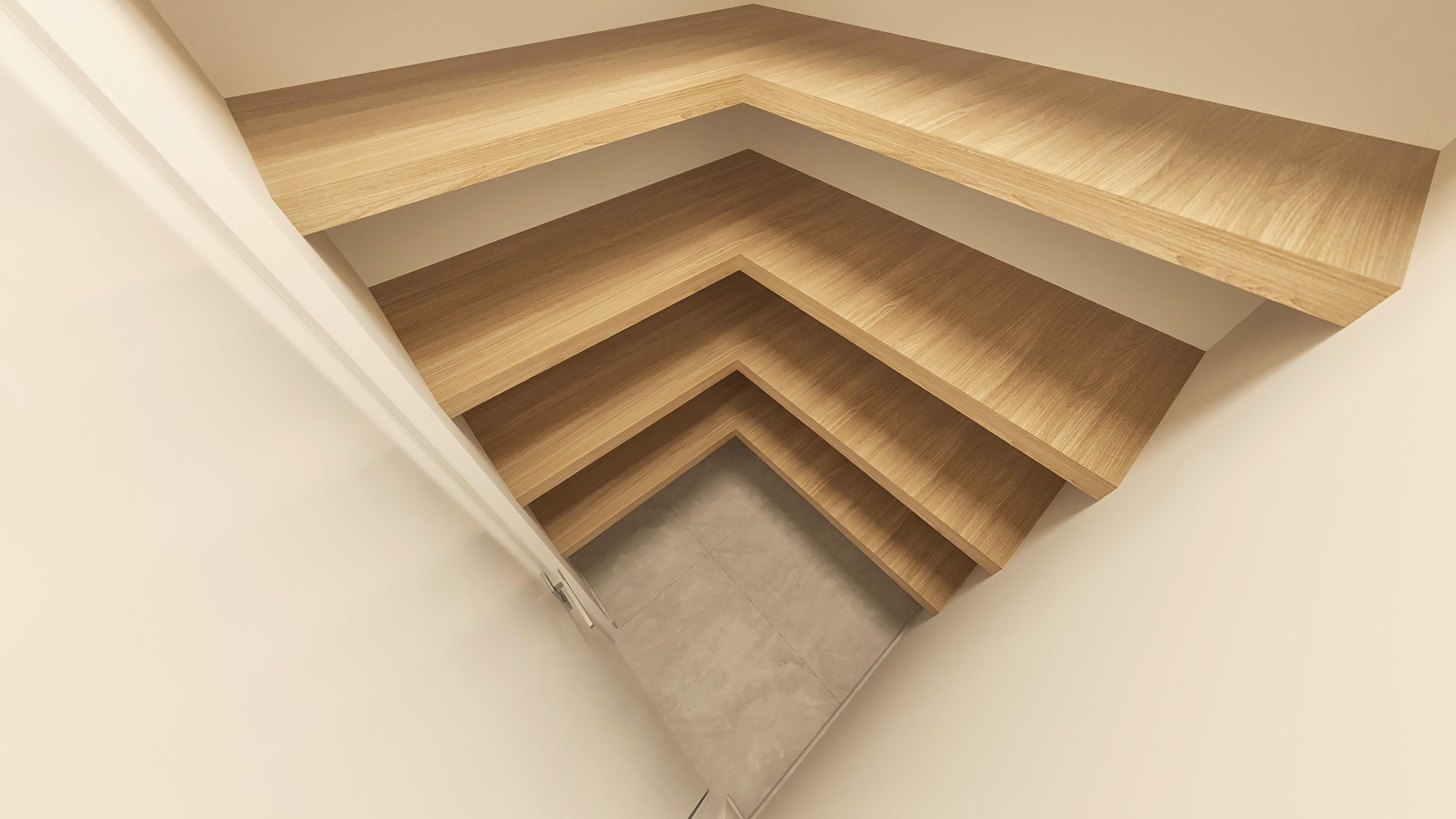 Detalle de escalones flotantes en madera con iluminación empotrada y suelo de cemento.
