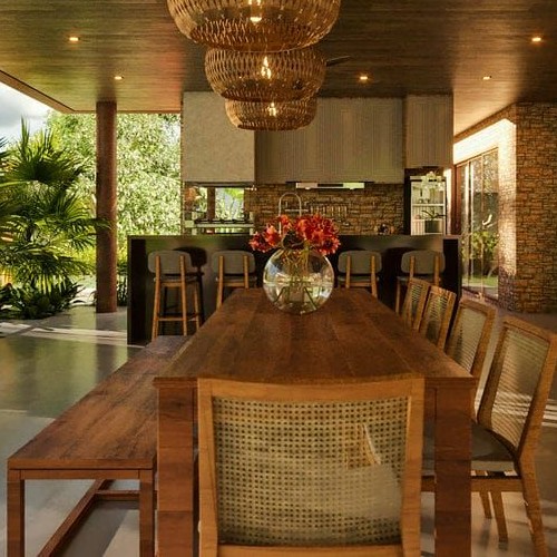 Projeto de área gourmet com mesa de madeira rústica, cadeiras em palha, balcão integrado e iluminação aconchegante, cercada por paisagismo exuberante.