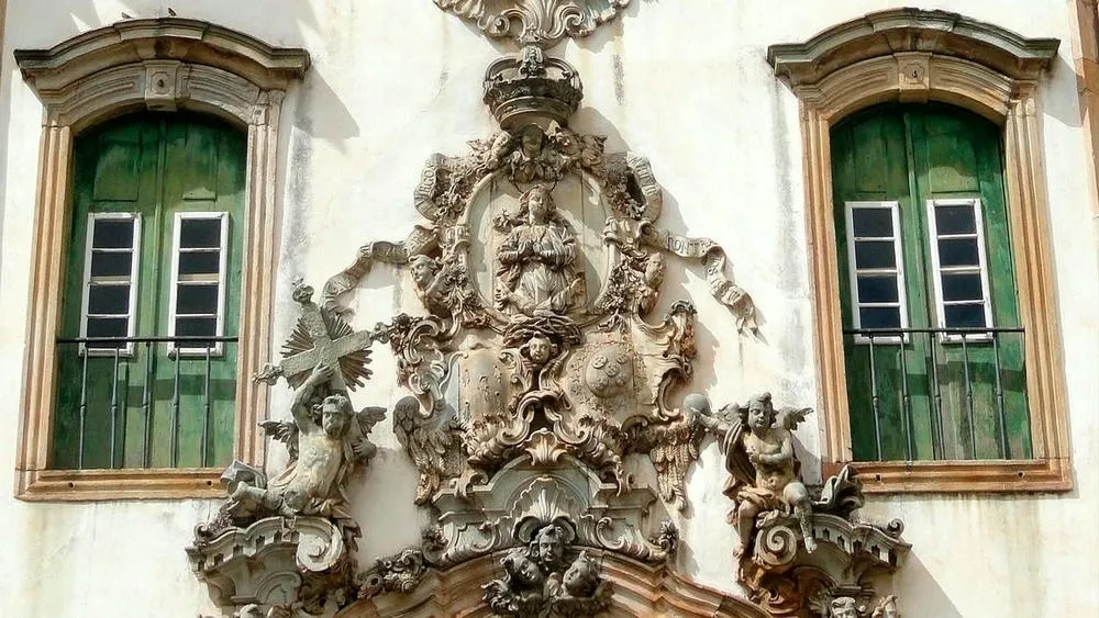 Fachada detalhada de uma igreja barroca no Brasil, com esculturas e portas de madeira.