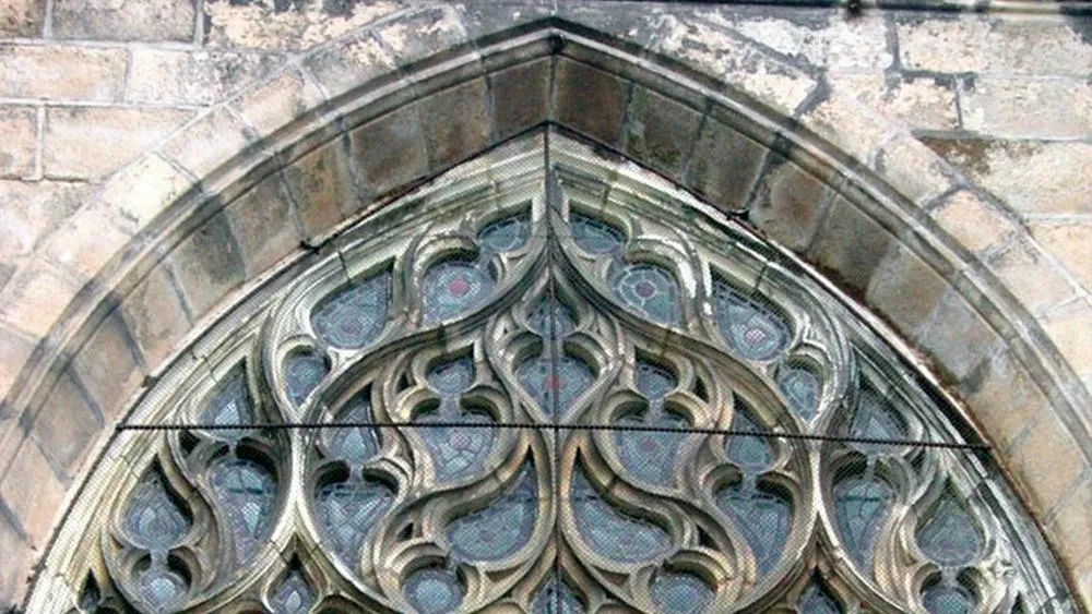 Arco ogival detalhado de uma janela gótica com vitrais coloridos e intrincados.