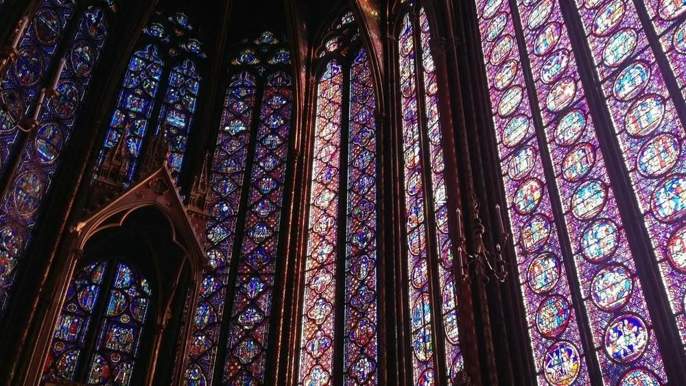 Vitrais coloridos e imponentes de uma capela gótica, preenchendo grandes janelas.
