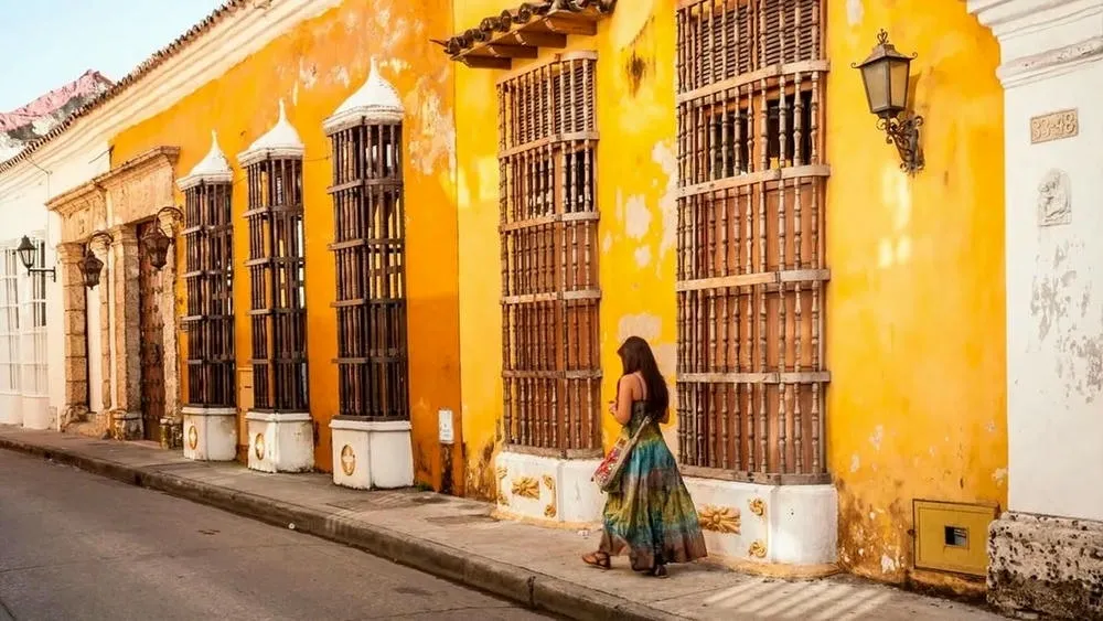 Rua colorida com casas em tons de amarelo e terracota, no estilo colonial mexicano, sob um céu azul claro.