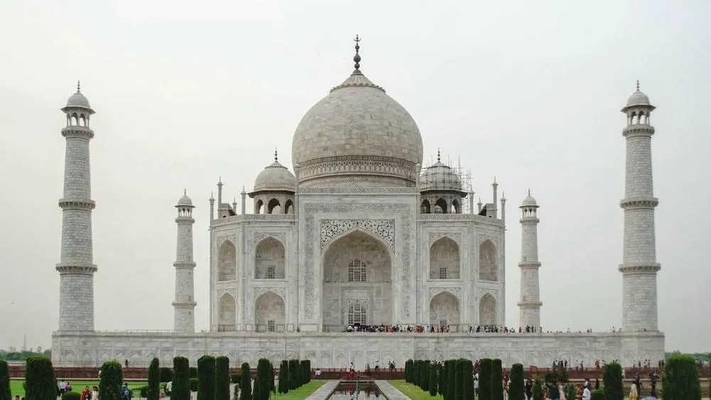 Vista frontal del Taj Mahal, con su imponente arquitectura en mármol blanco y cúpulas, rodeado por jardines y espejos de agua, simbolizando pureza y perfección en la arquitectura.