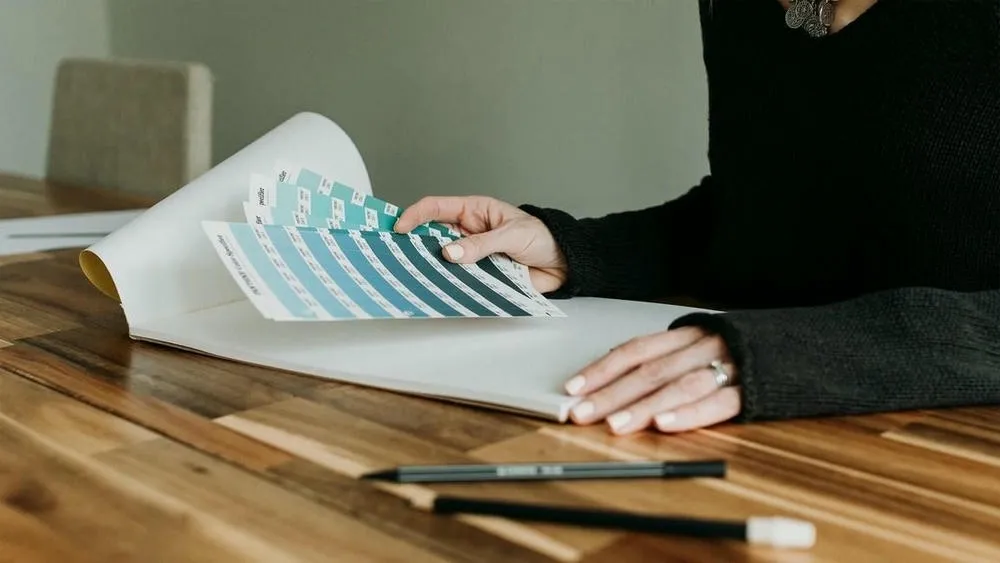 Un baño moderno con revestimientos en tonos de gris y azul claro, armario de madera, lavabo blanco y espejo grande. La iluminación es suave, y la presencia de la madera añade un toque de calidez al ambiente frío.