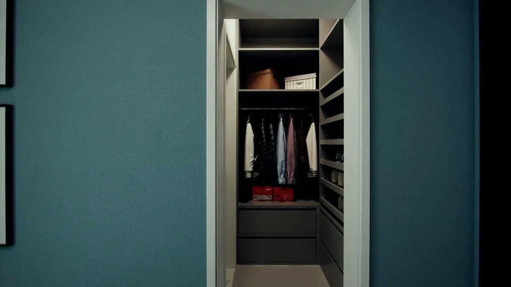 Vestidor pequeño y estrecho con estantes oscuros y ropa colgada, enfocado en almacenamiento vertical.