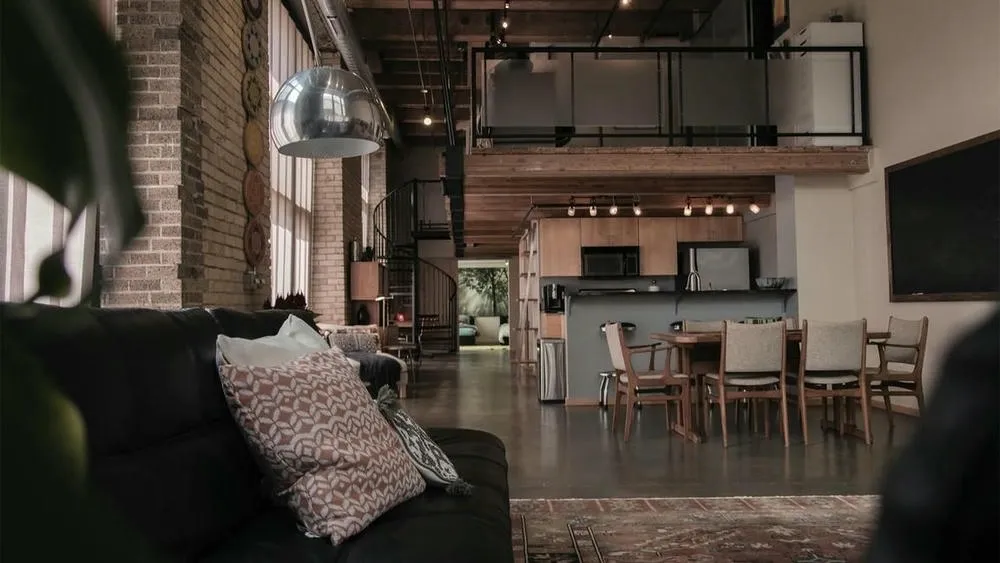Sala de estar e cozinha integradas em um ambiente com grandes janelas e piso de cimento queimado, exemplificando o conceito aberto em estilo industrial.