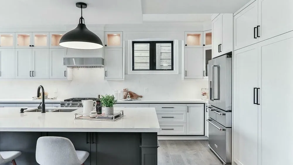 Uma cozinha moderna com armários brancos, bancada de quartzo, pia com torneira preta e ilha central com banquetas de madeira, ilustrando a funcionalidade e praticidade do design escandinavo.