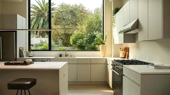 Cozinha moderna com armários brancos, ilha central e grandes janelas, seguindo um layout eficiente e minimalista.