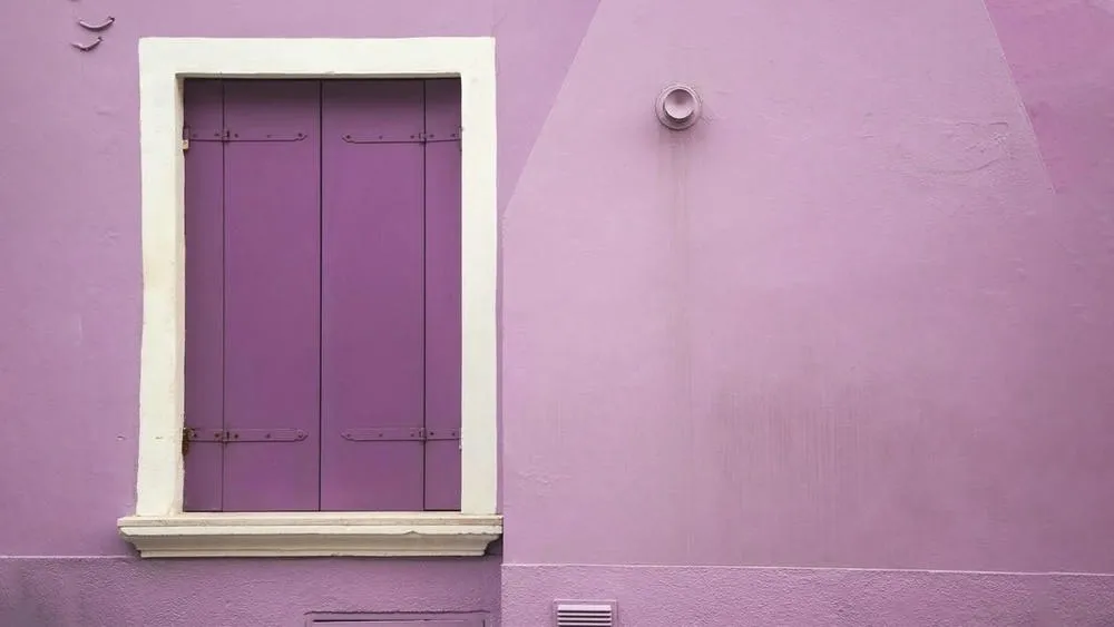 Un dormitorio con pared morada y cama con cabecero negro, decorado con luces de hadas y una manta peluda. La iluminación suave crea una atmósfera misteriosa y acogedora, con elementos que evocan la espiritualidad y creatividad.