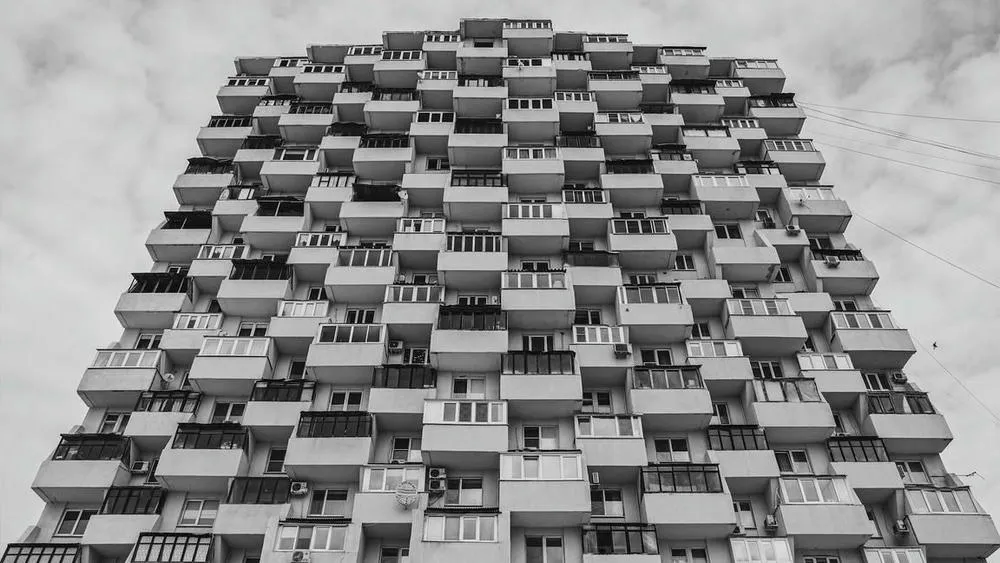 Detail of a brutalist building facade in black and white, showing the repetition of concrete blocks with square windows and rough texture.