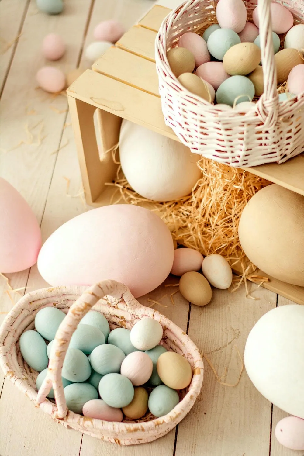 Baskets full of pastel-toned Easter eggs (pink, blue, beige), arranged on a light wooden surface with straw.