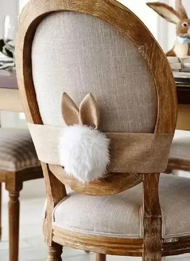 Wooden chair with light upholstery, decorated on the back with a white pompom tail and bunny ears.