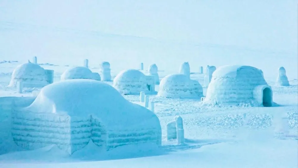 Multiple igloos built in the snow, with mountains and clear sky in the background.