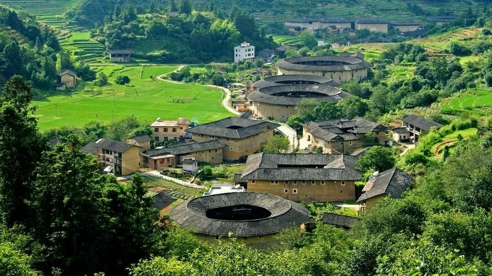 Várias construções circulares e retangulares, conhecidas como Tulou, entre vegetação verde, na província de Fujian, China.