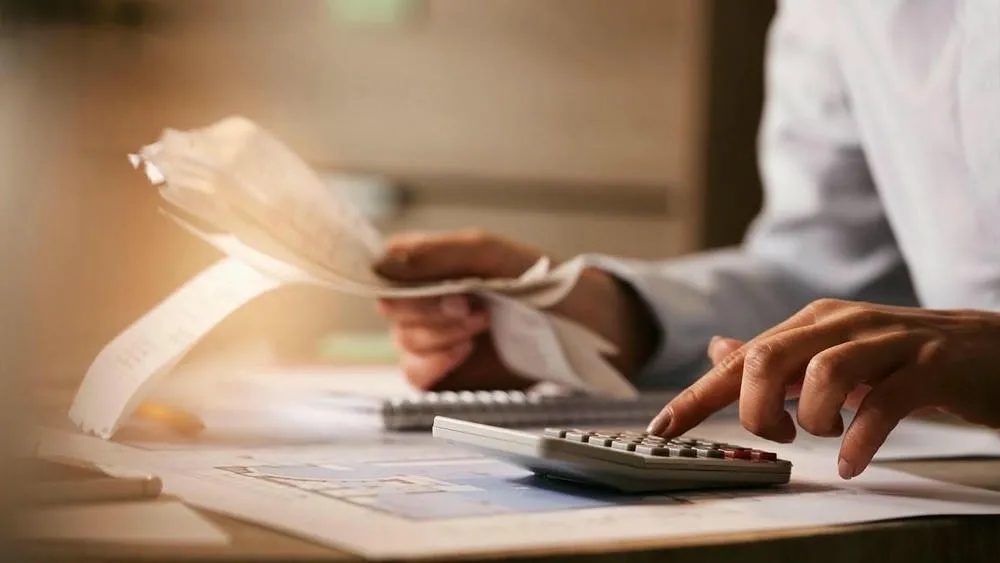 Hands of a person using a calculator and holding papers, symbolizing the cost calculation of a roof project.