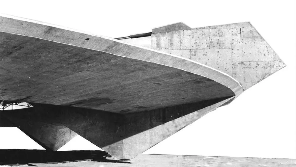 Bottom view of an architectural structure of exposed concrete, with robust shapes and geometric lines, characteristic of brutalist architecture.
