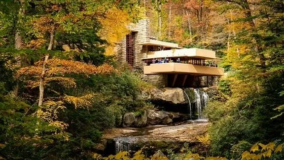 Fallingwater House amidst trees with autumn foliage, with the waterfall flowing below the structure.
