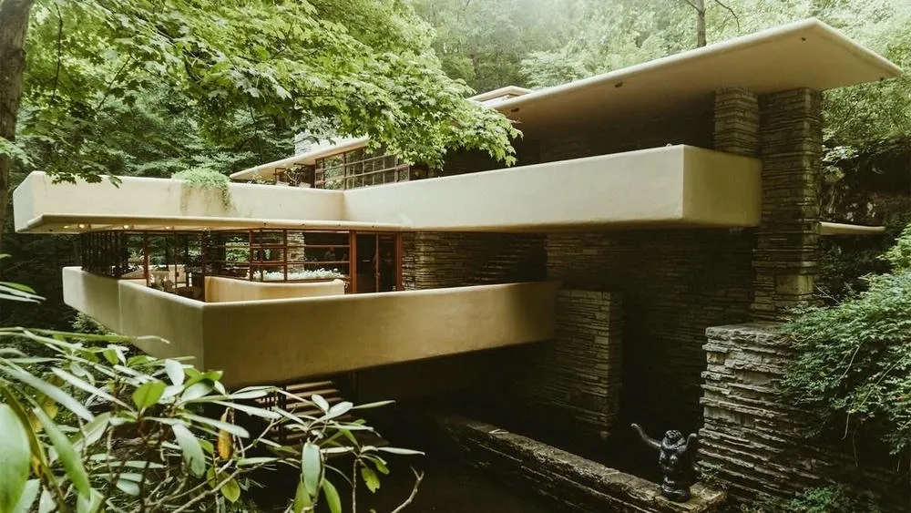 Fallingwater house inserted in nature with its cantilevered slabs over the waterfall, surrounded by trees with autumn foliage.