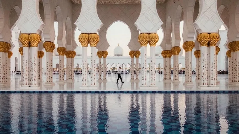 La Gran Mezquita Sheikh Zayed en Abu Dabi, con sus minaretes y cúpulas blancas, rodeada de espejos de agua que la reflejan.