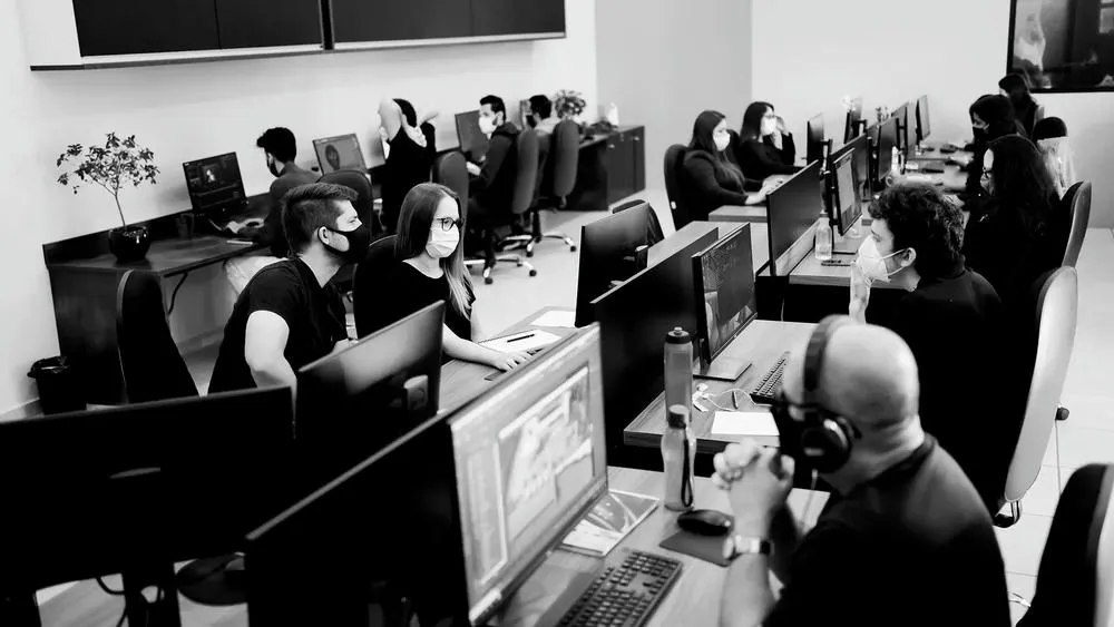 Modern office with several people working on computers, some wearing masks, in an interior design environment.