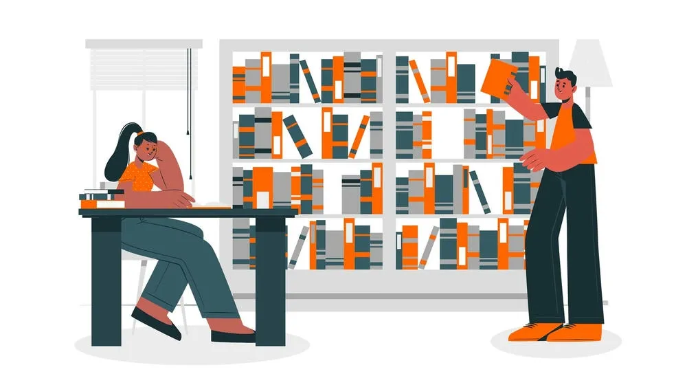 Person sitting studying at a table with books, while another person takes a book from a full bookshelf.