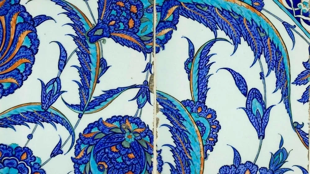 Details of blue and intricate tiles on a wall that is part of Islamic architecture, with geometric and floral patterns. Light falls on the surface, highlighting the texture and shades of blue.