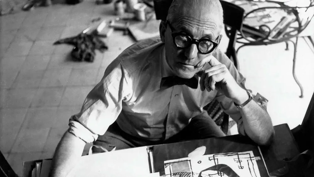 Retrato em preto e branco de Le Corbusier, arquiteto famoso, inclinando-se sobre um desenho.