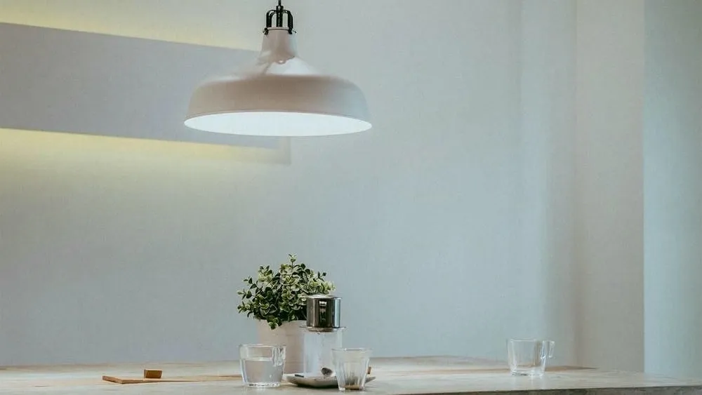 Modern pendant light fixture in a bright environment with a small plant in the center of the table, showing how artificial lighting can complement natural light to create a welcoming space.