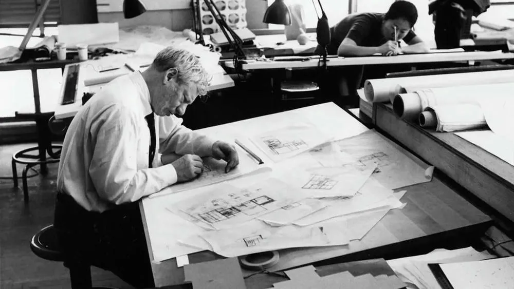 Retrato em preto e branco de Louis Kahn, arquiteto famoso, desenhando em uma prancheta em seu escritório.