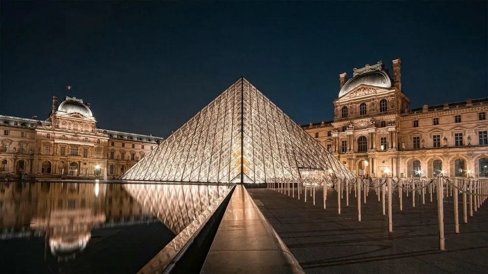La pirámide de vidrio del Museo del Louvre en París, Francia, reflejada en un espejo de agua al atardecer.